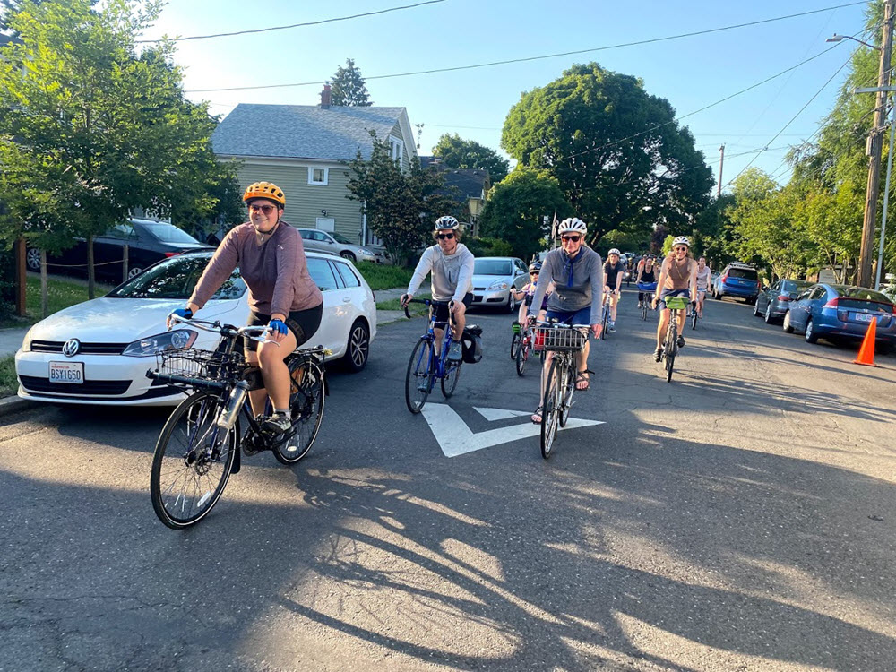 Image of a group bicycle ride, with several people on bikes with helmets on a neighborhood street