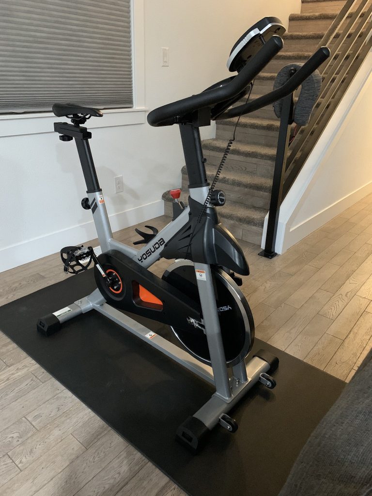 A stationary bike on a mat in a house in front of stairs