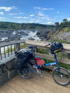 A blue Bike Friday bike loaded up with panniers and touring gear in front of a background of a large waterfall